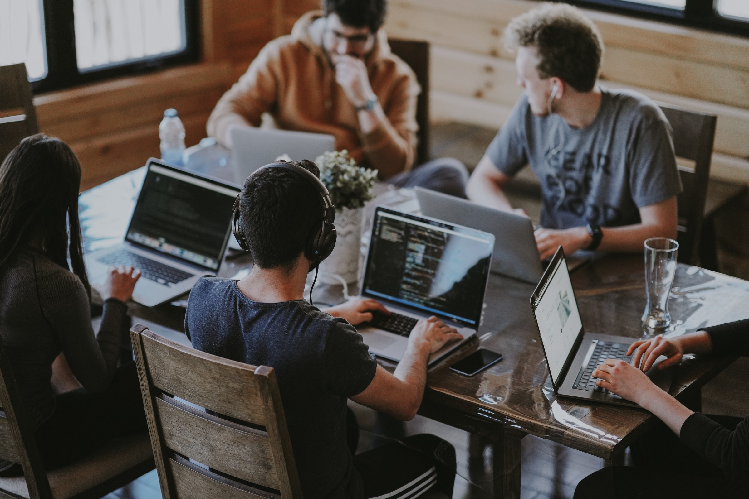 5 people sitting around a wooden table working on laptops and collaborating together.